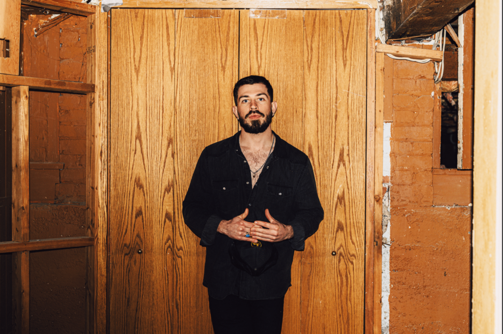 Singer stands by wooden door.